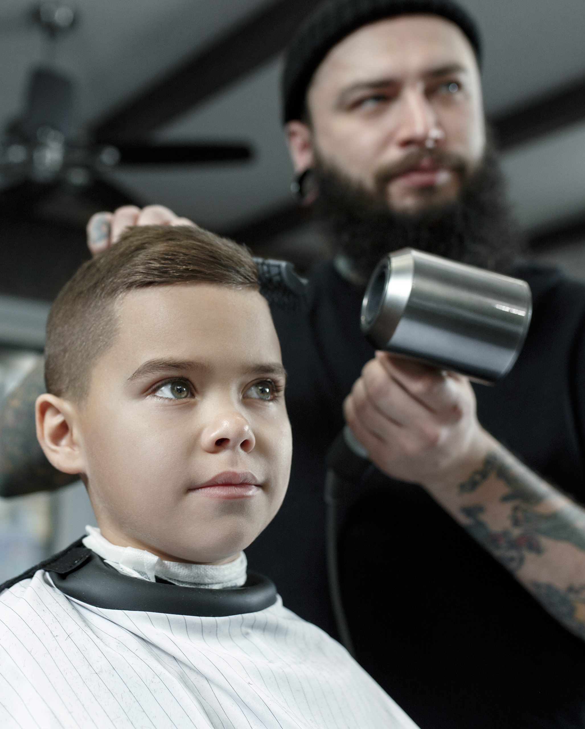Children hairdresser cutting little boy against a dark background.